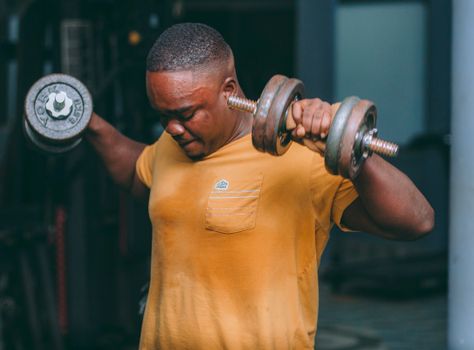 Young man in gym lifting dumbbells, showcasing strength and dedication to fitness.