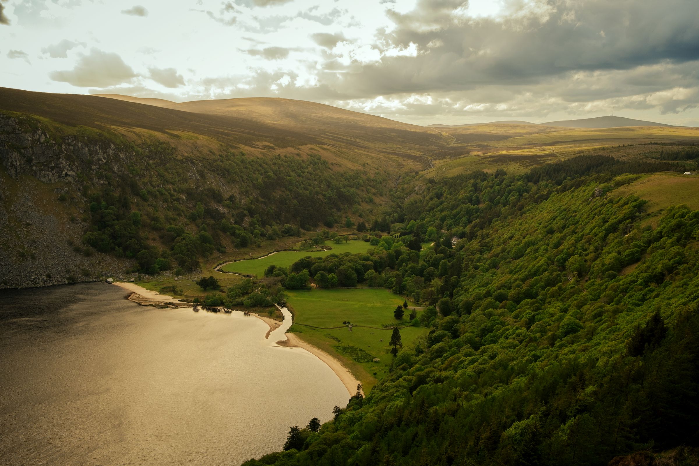 A aerial view of a valley with greenery, a river, and mountains in County Wicklow, Ireland