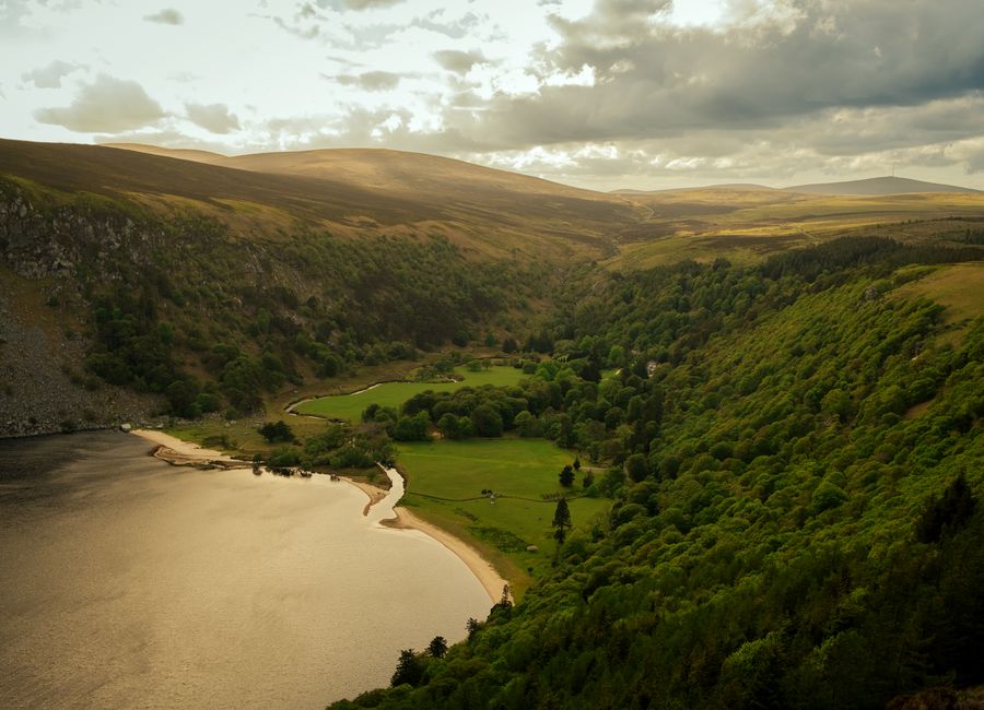 A breathtaking aerial view of a tranquil valley with lush greenery, a river, and mountains in County Wicklow, Ireland.
