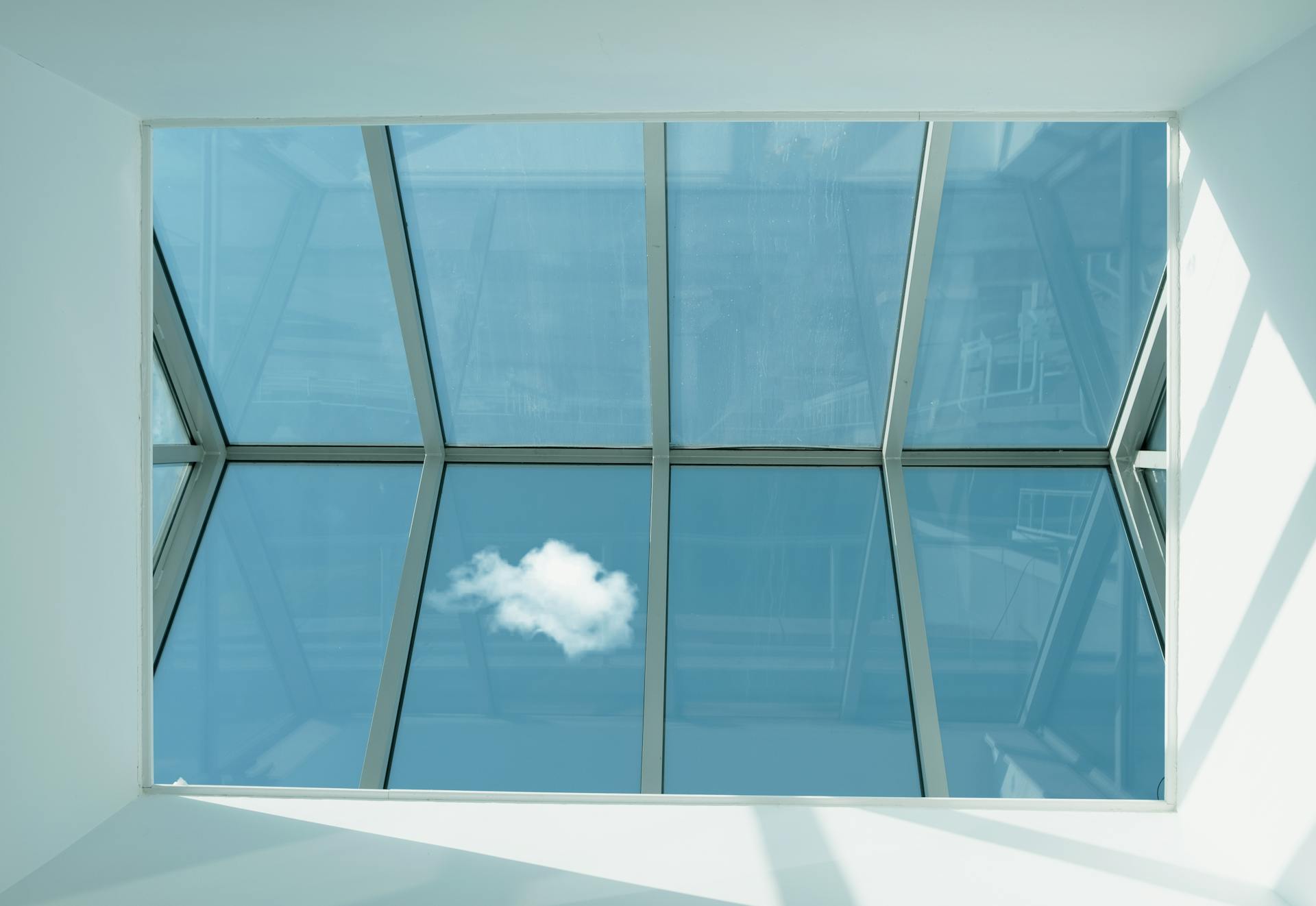 Contemporary skylight showcasing a clear blue sky and a single cloud reflection.