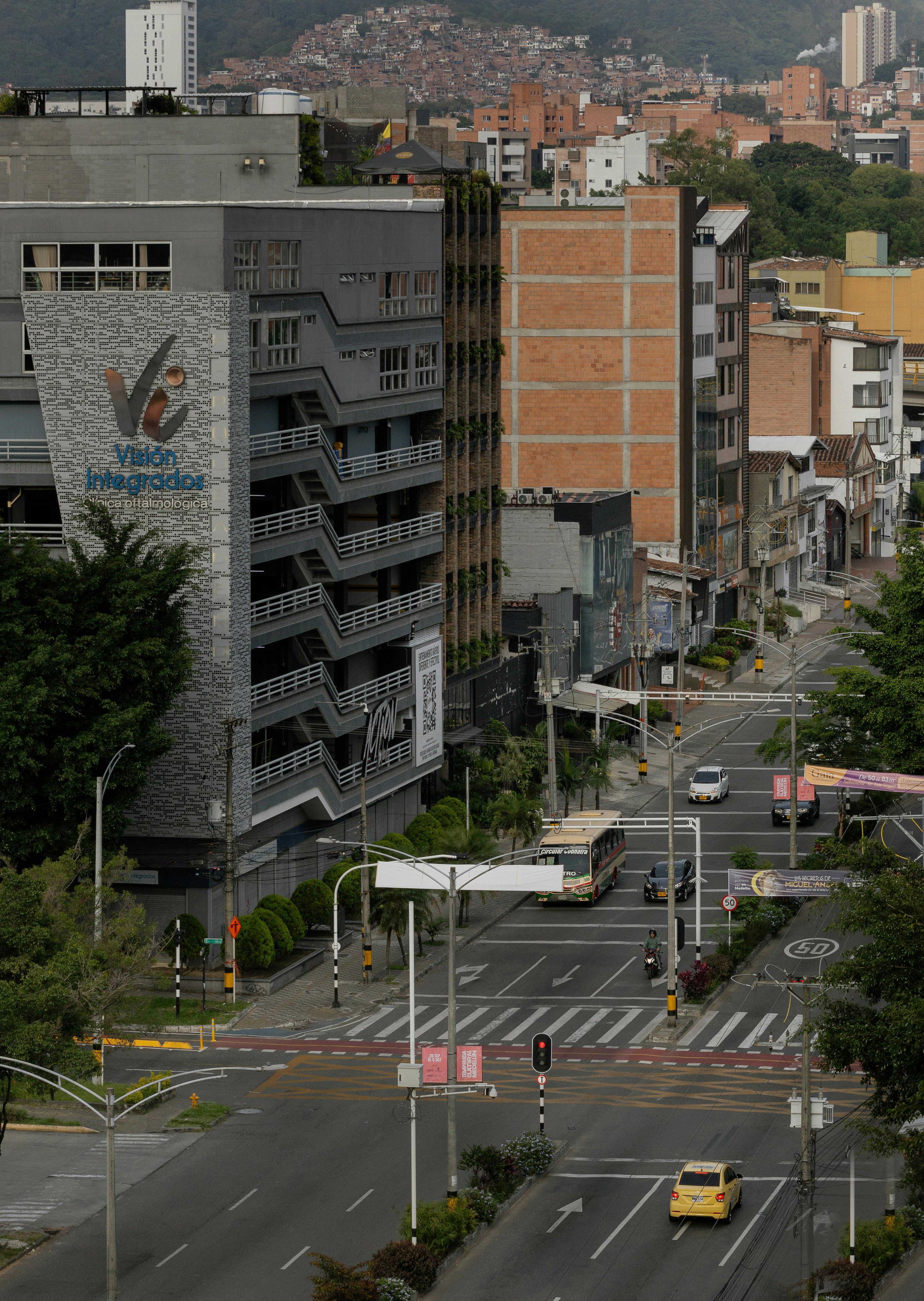 City street in Medellín, Colombia showing buildings, cars, and a hilly background.