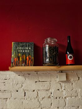 Rustic shelf with a cookbook, jar, and wine bottle against a red wall.