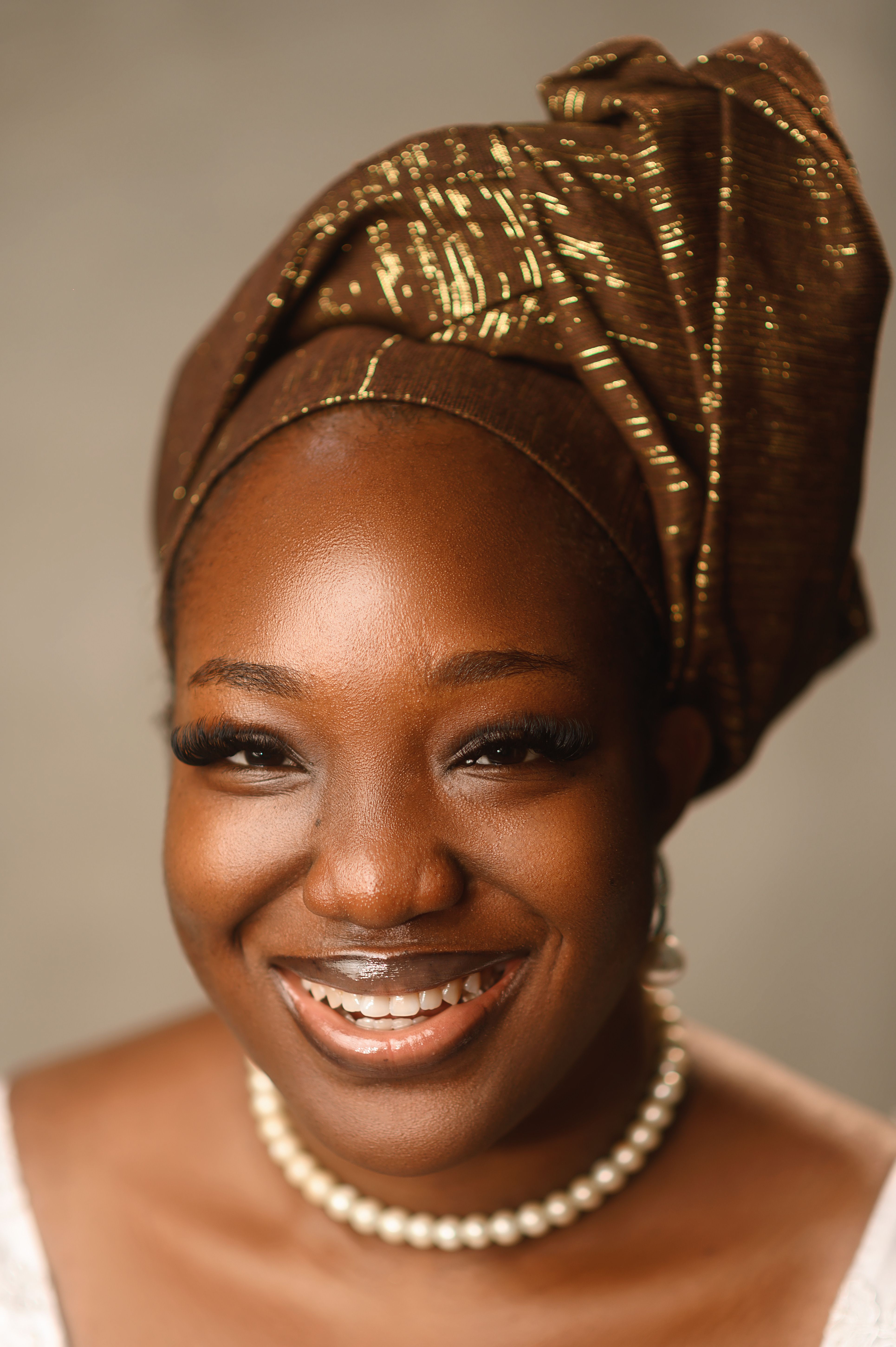 Portrait of a smiling woman in a traditional headwrap and pearl necklace, exuding elegance.
