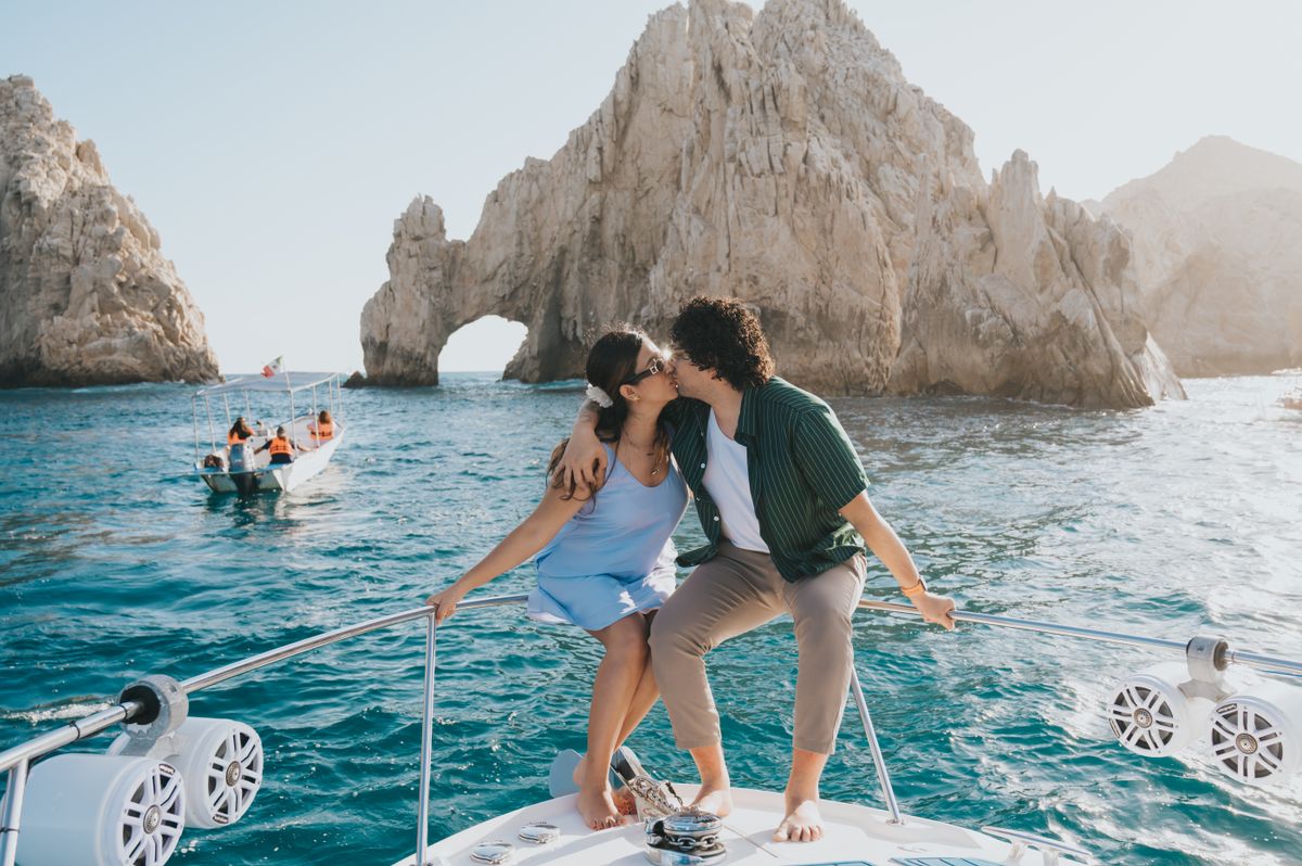 Una pareja comparte un beso romántico en una lancha cerca del icónico Arco de Cabo San Lucas