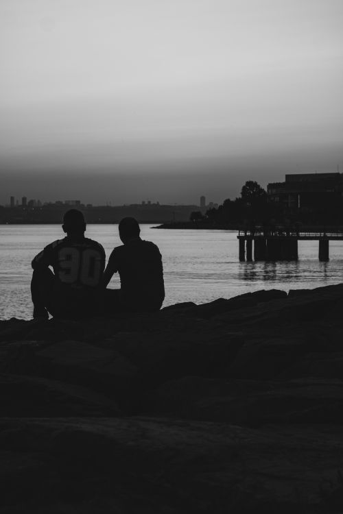 Free Two Men Sitting on a Rock Watching the Sea Stock Photo