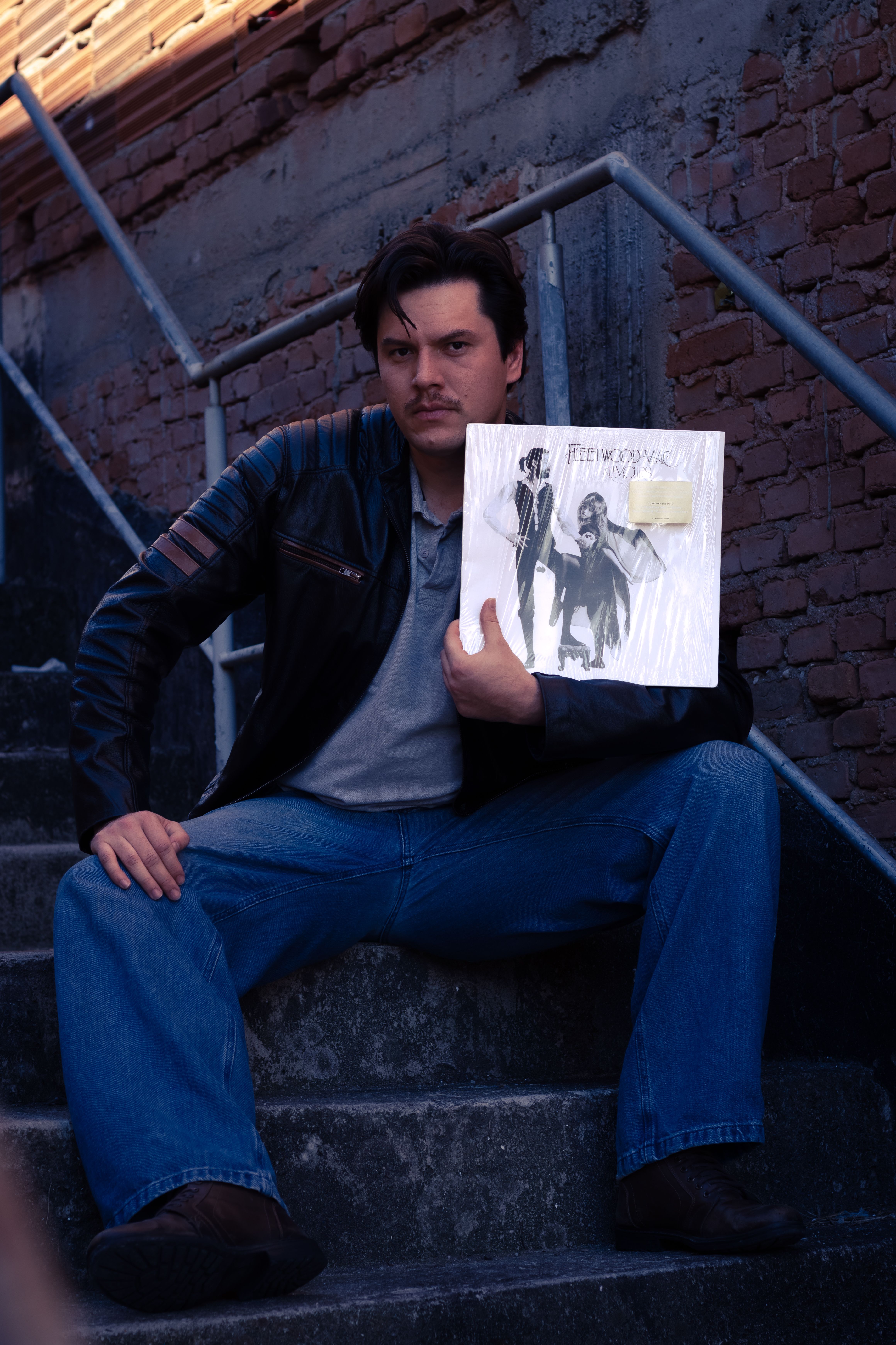 A man in casual attire holds a vinyl record while sitting on a stone staircase.