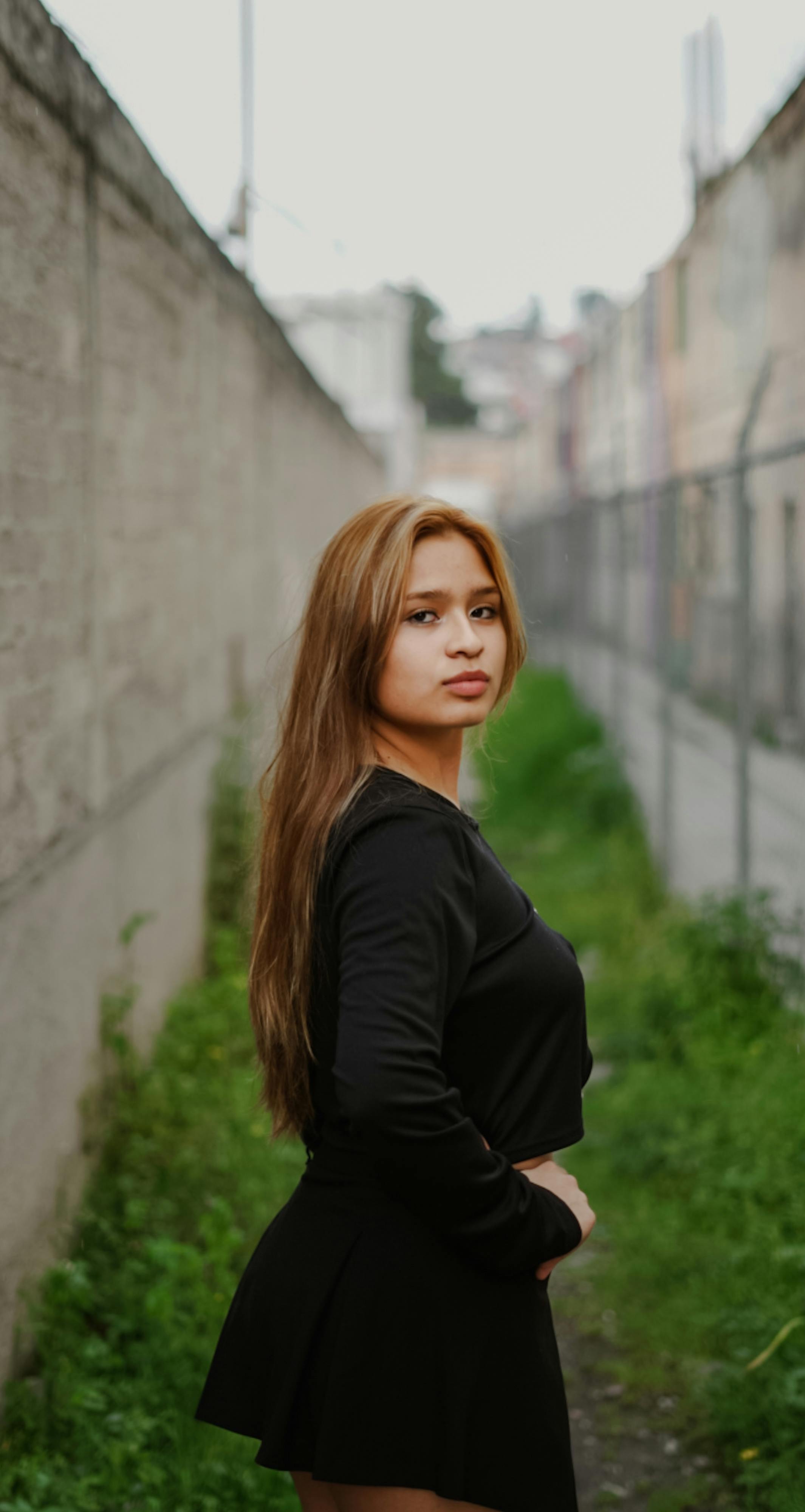 Side portrait of a woman standing confidently in an urban alleyway wearing a black outfit.
