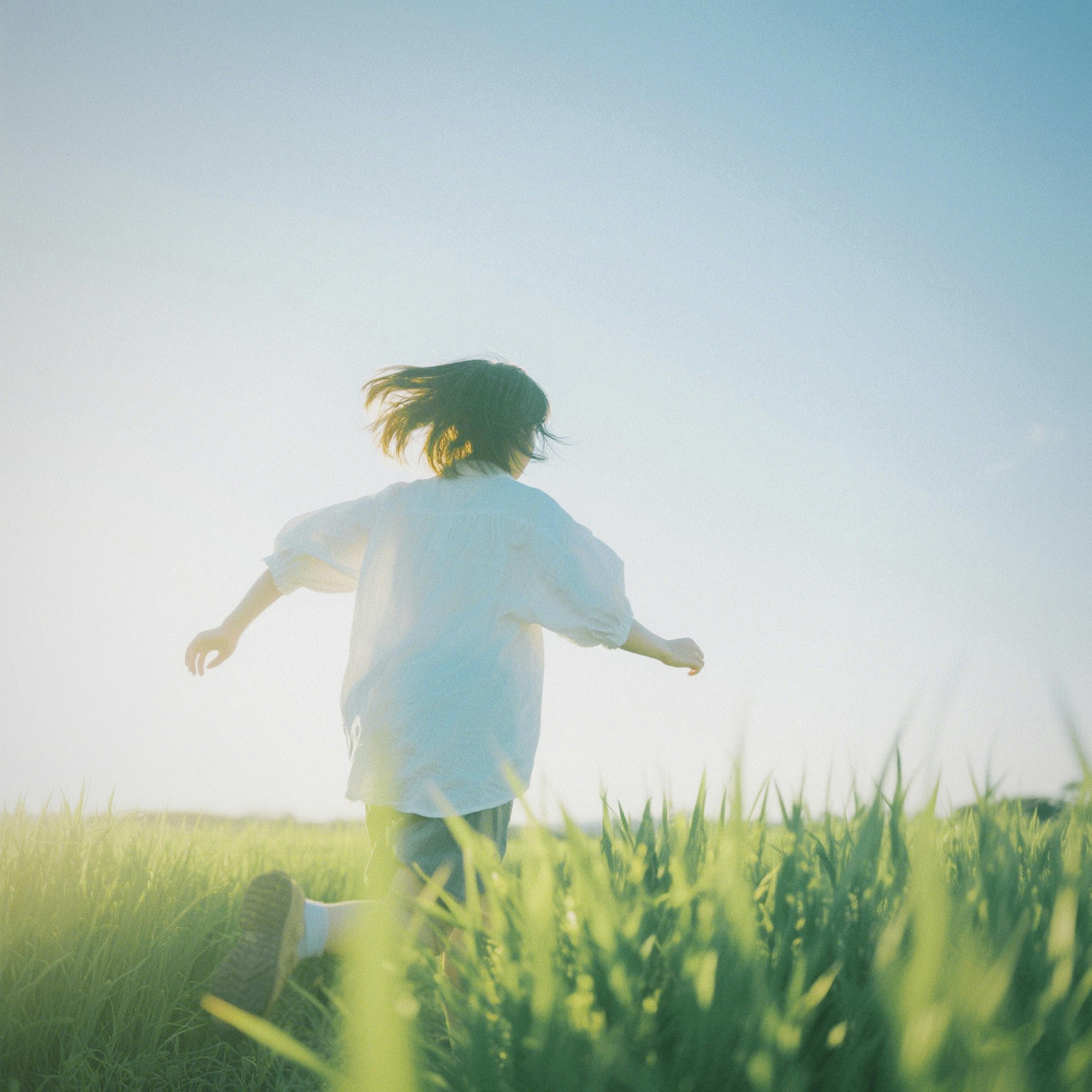 Child running freely through a bright green field under a clear blue sky.