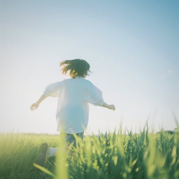 Child running freely through a bright green field under a clear blue sky.