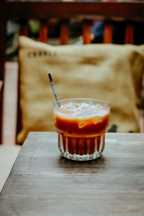 Free A cold iced coffee with a straw, resting on a rustic wooden table outdoors. Stock Photo
