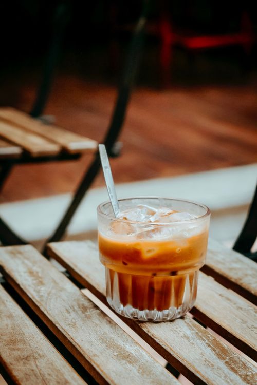 Free A refreshing glass of iced coffee sits on a wooden table in an outdoor cafe setting. Stock Photo