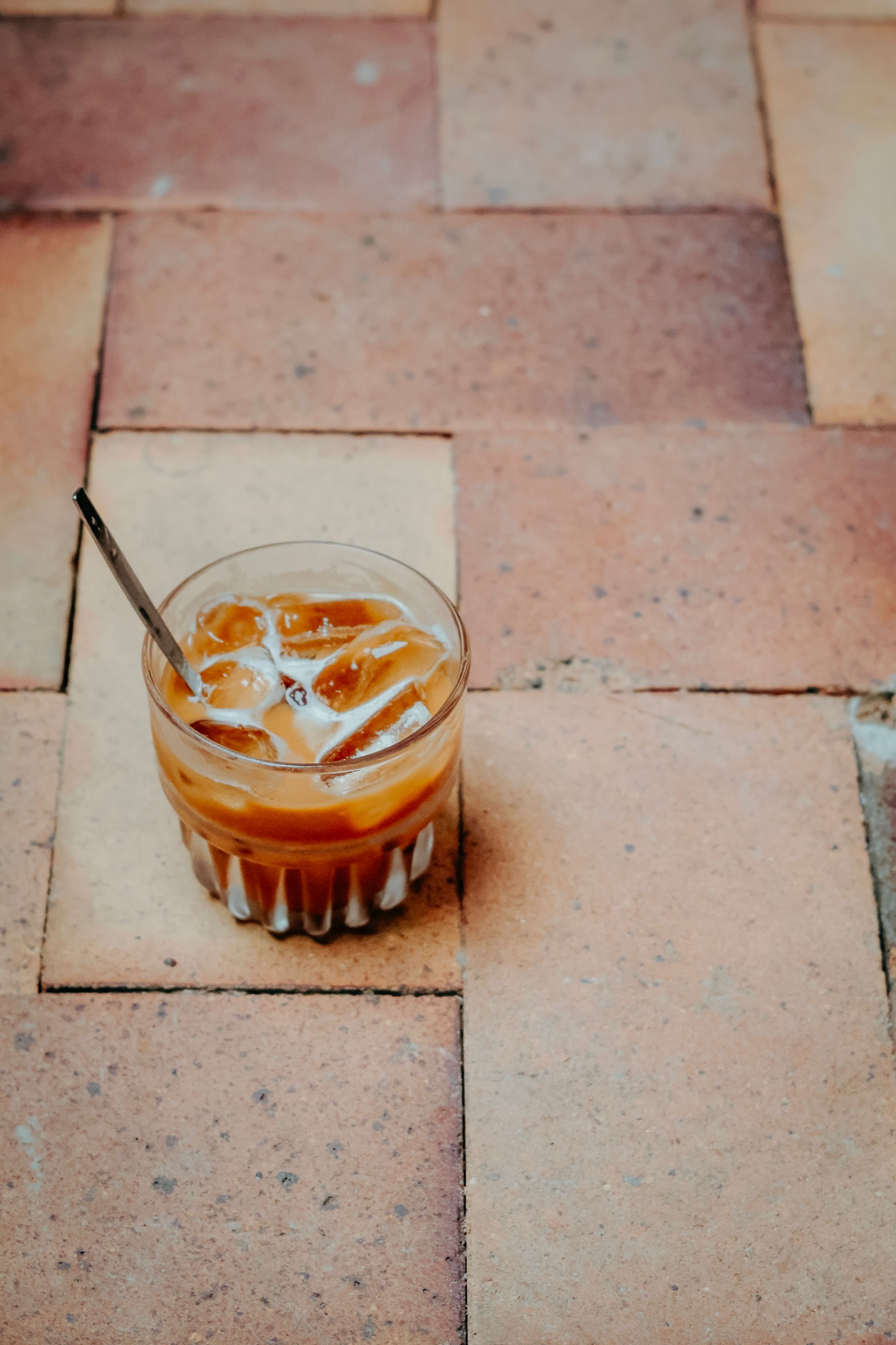 A glass of iced coffee with a straw on a rustic outdoor tile surface.