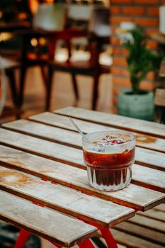 A refreshing glass of iced coffee sits on a rustic wooden table at an outdoor cafe.
