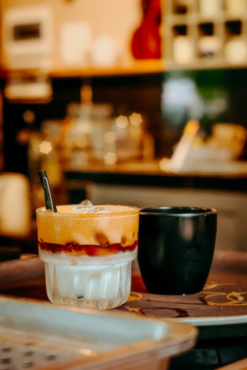 Free A refreshing iced coffee with layers alongside a black cup in a cozy cafe setting. Stock Photo