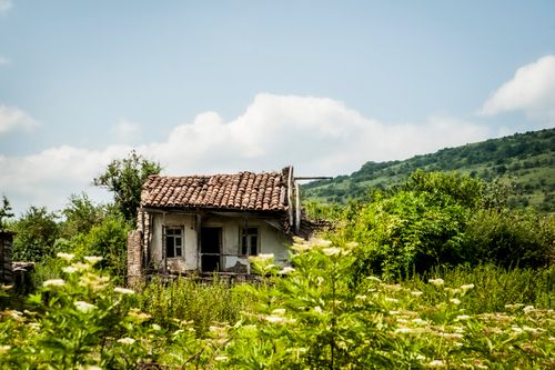Free An old, abandoned house amidst lush greenery and rolling hills under a bright blue sky. Stock Photo