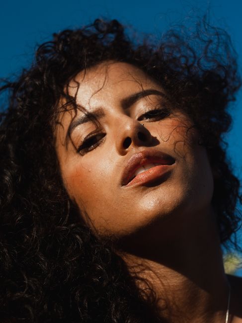 A captivating close-up portrait of a woman with curly hair under a clear blue sky, showcasing natural beauty.