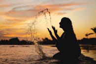 日落时分，一名女子在海滩上泼水的剪影，轮廓宁静而充满活力