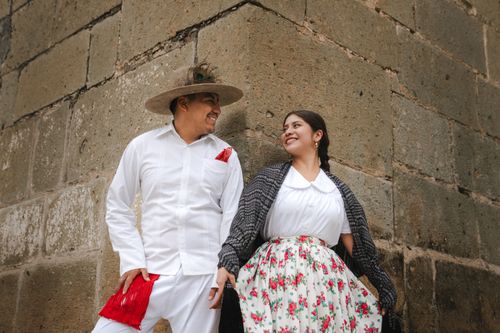 Free A joyful couple in traditional Mexican attire posing against a rustic stone wall in Oaxaca. Stock Photo