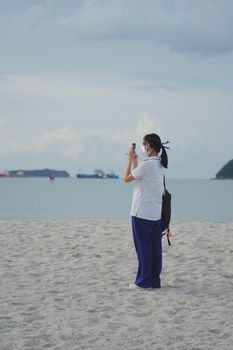 A woman in a mask captures beach views with her smartphone. Seascape and serenity.