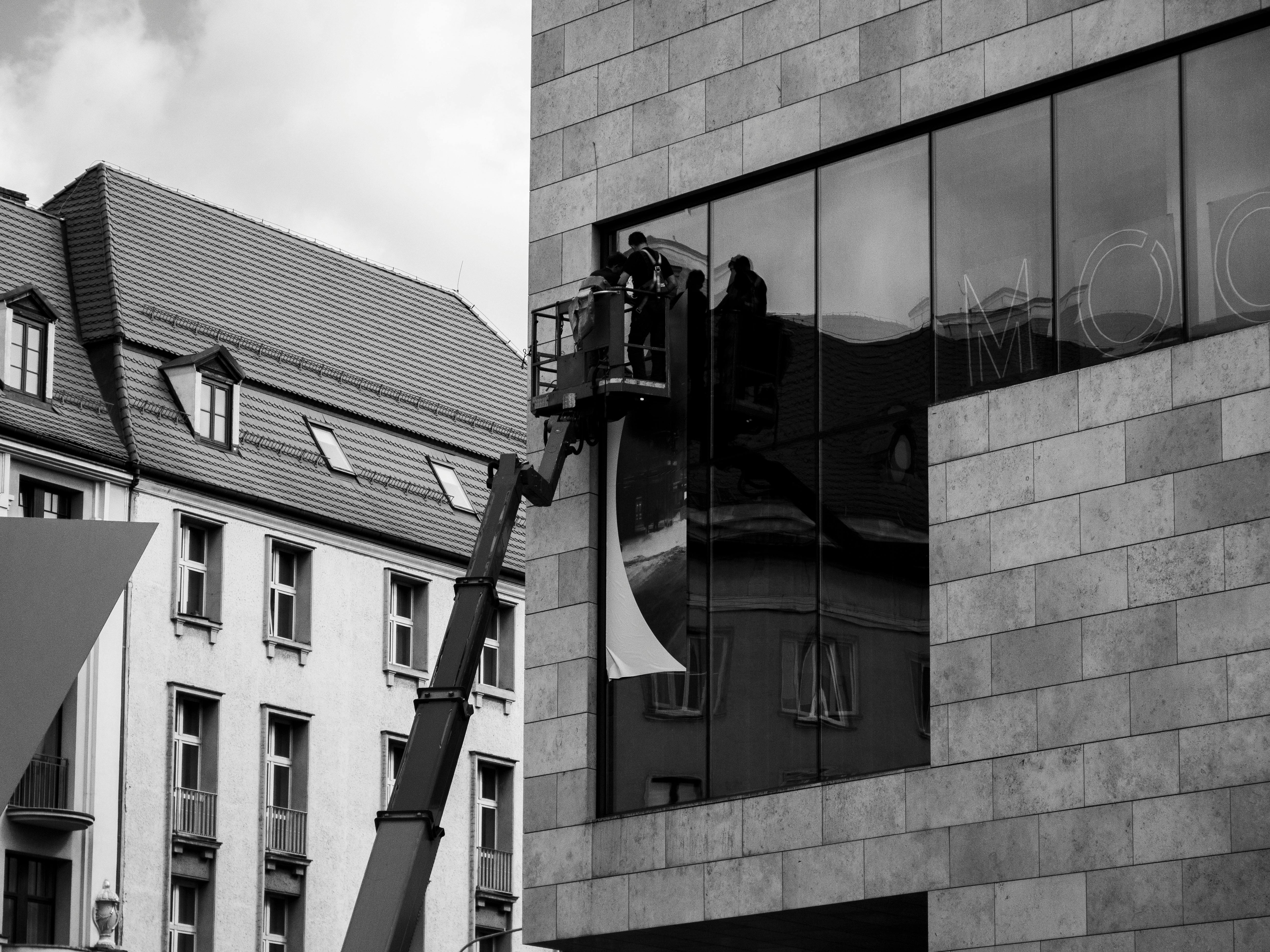 Black and white photo of workers using a lift to install a glass panel on a modern building exterior.