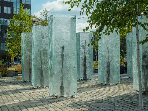 Free Artistic glass sculpture installation in a sunny urban park setting, surrounded by trees. Stock Photo