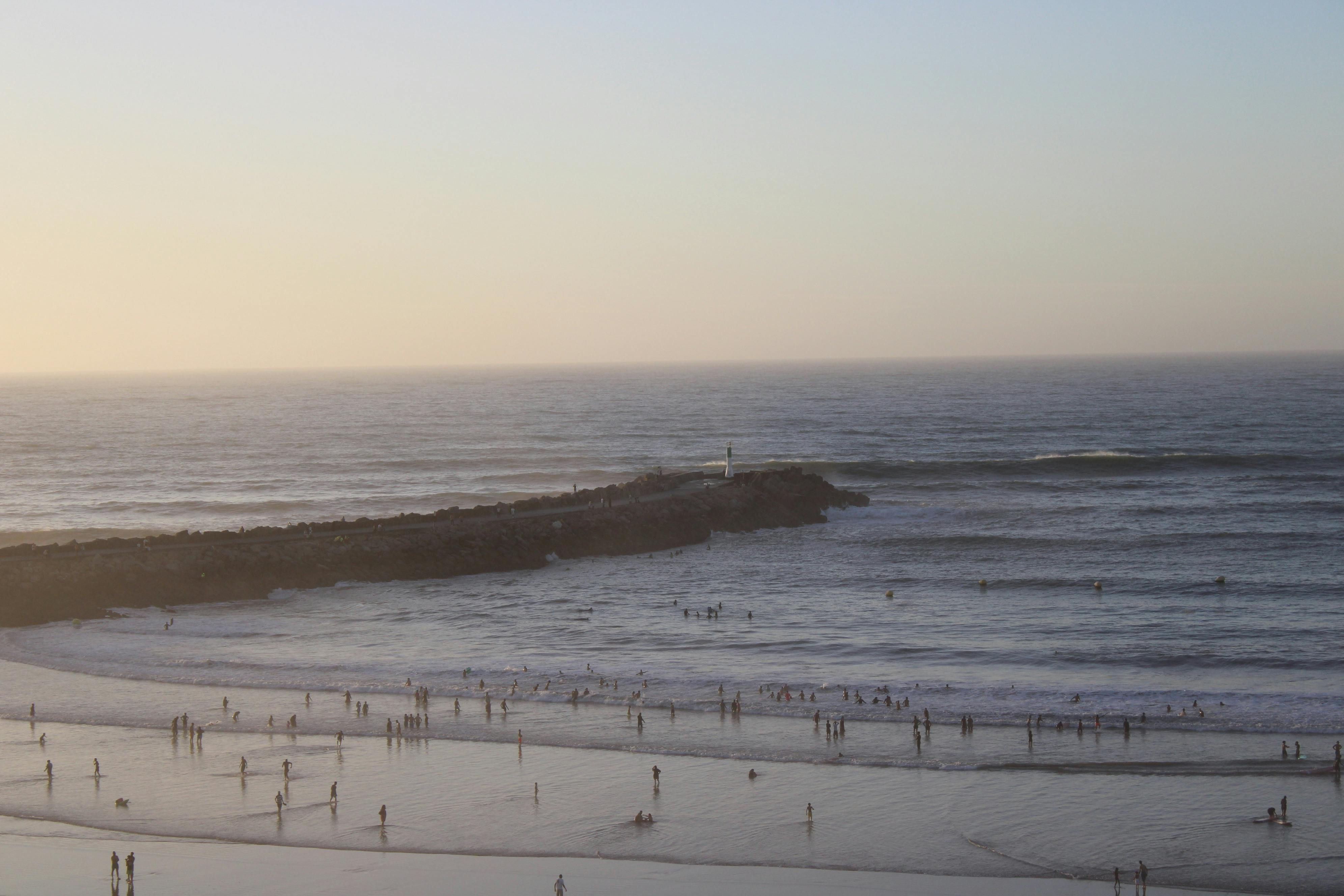 Serene view of Rabat beach during sunset with silhouettes of people enjoying the water.