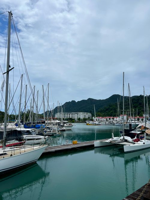 Free Peaceful marina with yachts docked under cloudy sky and lush mountains in the distance. Stock Photo