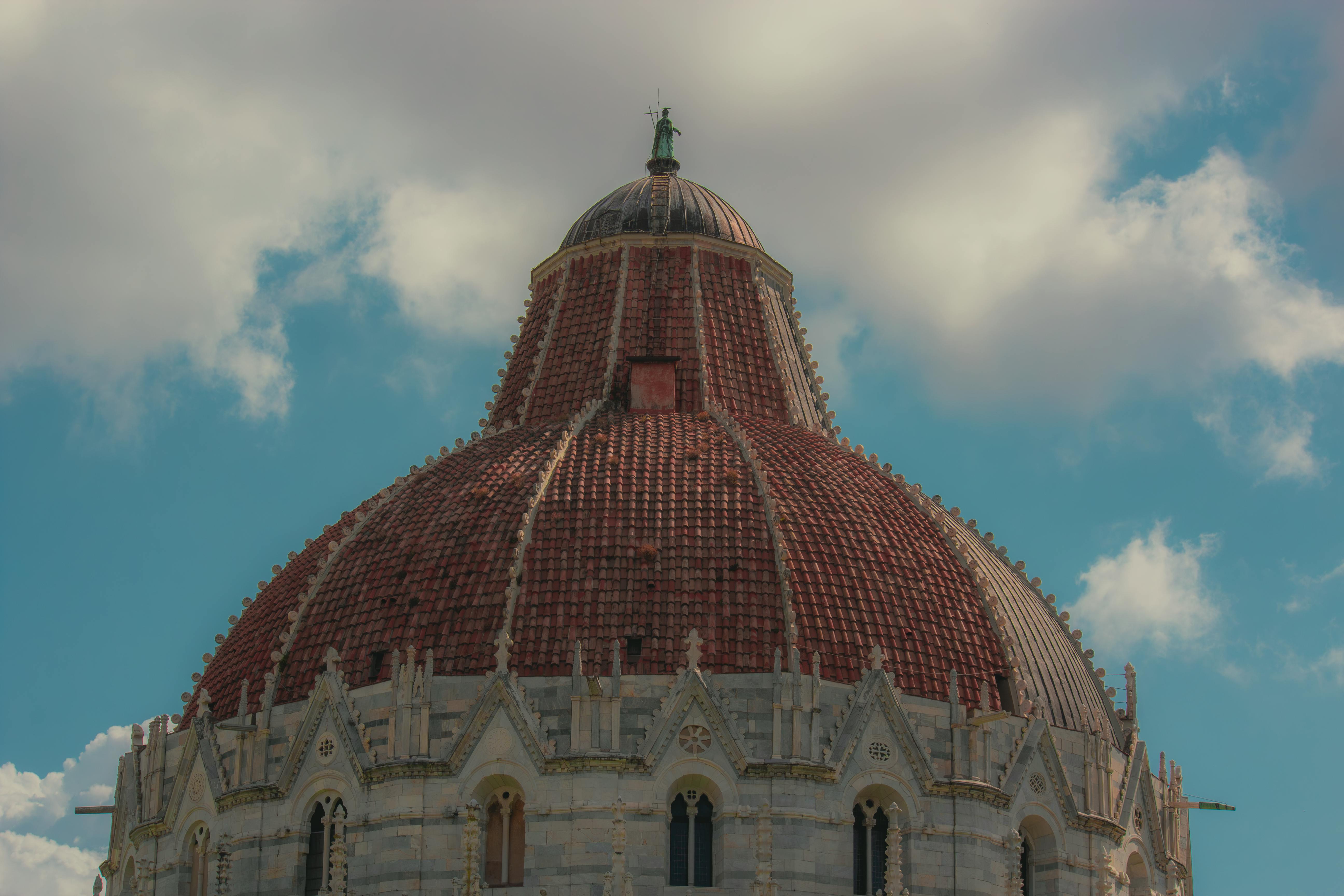 Captivating view of the iconic dome of Pisa Baptistery against a bright blue sky with fluffy clouds.