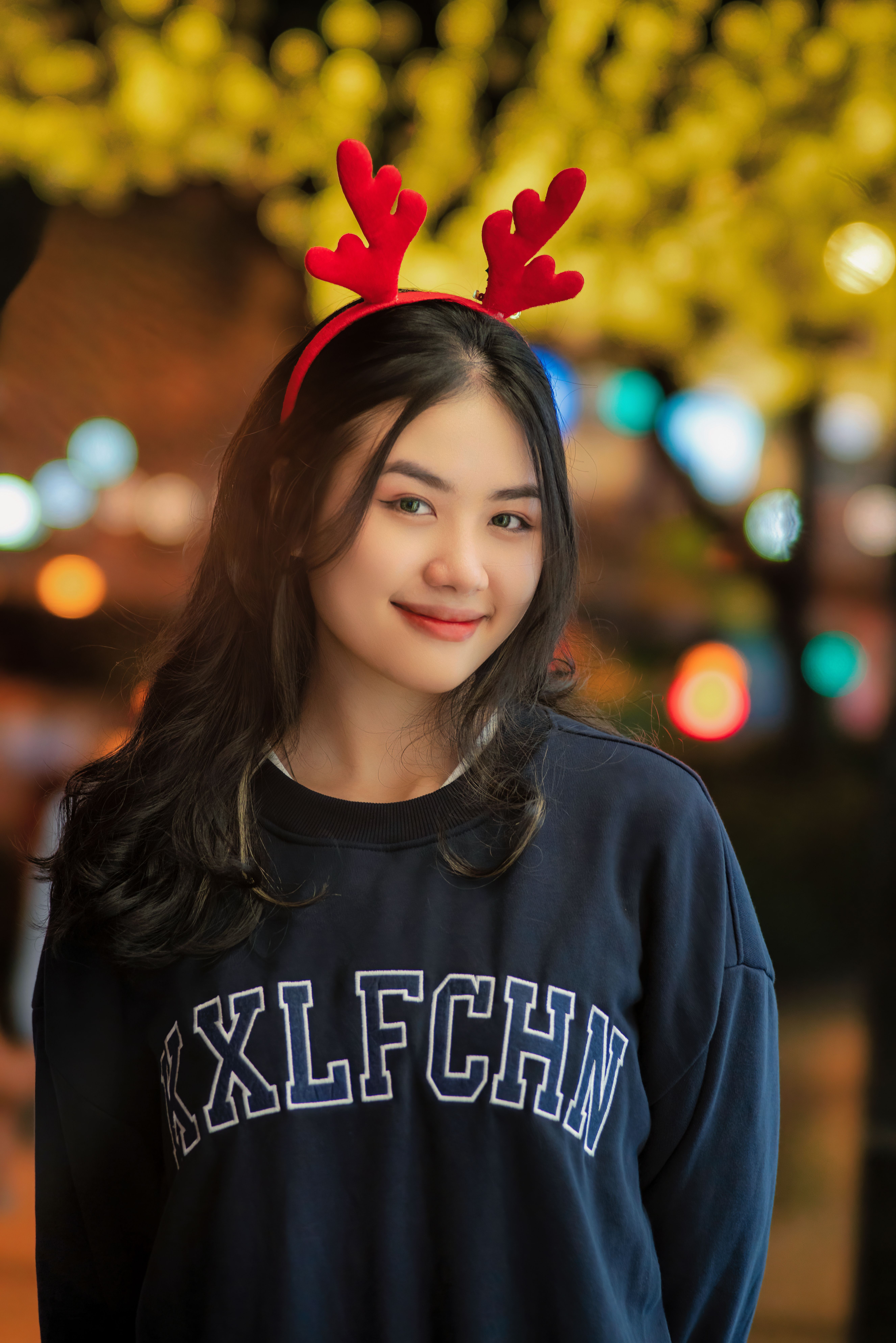 A young woman smiling while wearing a festive red reindeer headband indoors.