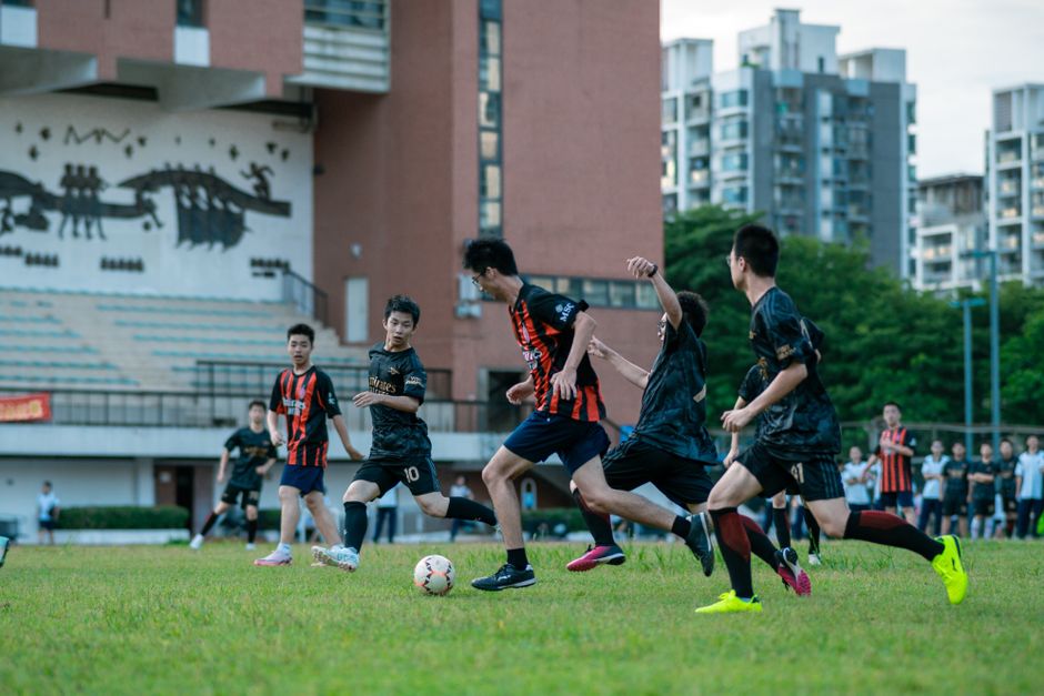 Teenagers playing a competitive soccer match on a urban outdoor field.