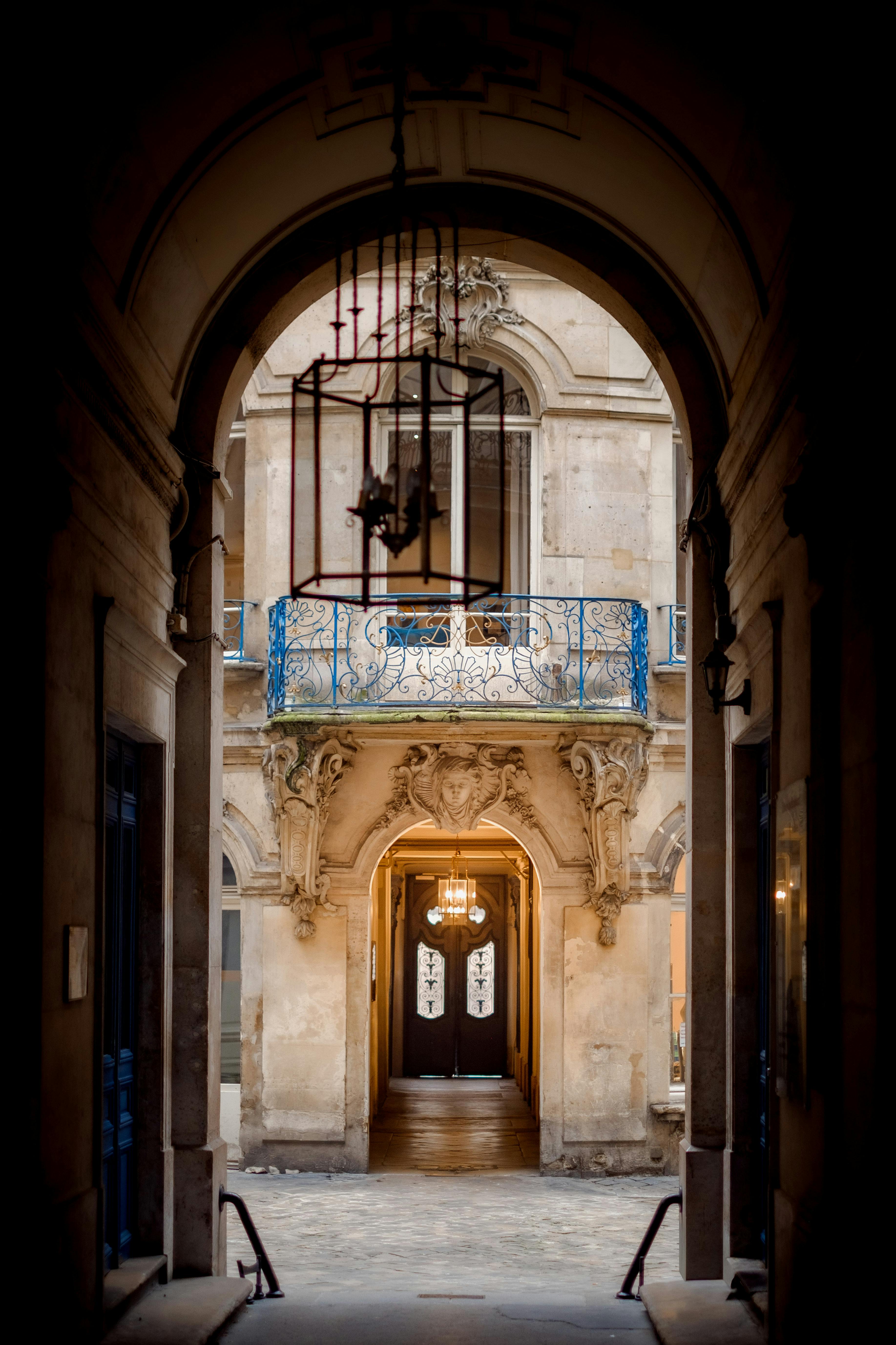 View through an elegant arched passage leading to a historic building entrance with ornate detailing.