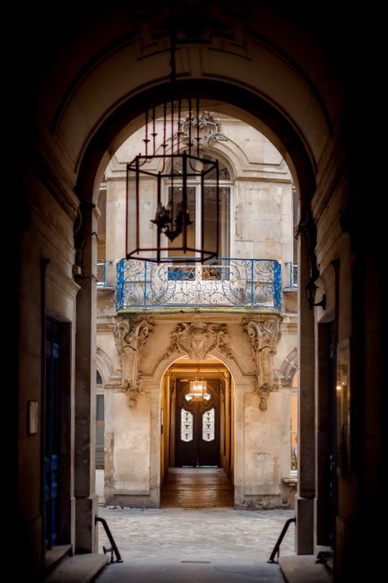 View through an elegant arched passage leading to a historic building entrance with ornate detailing.