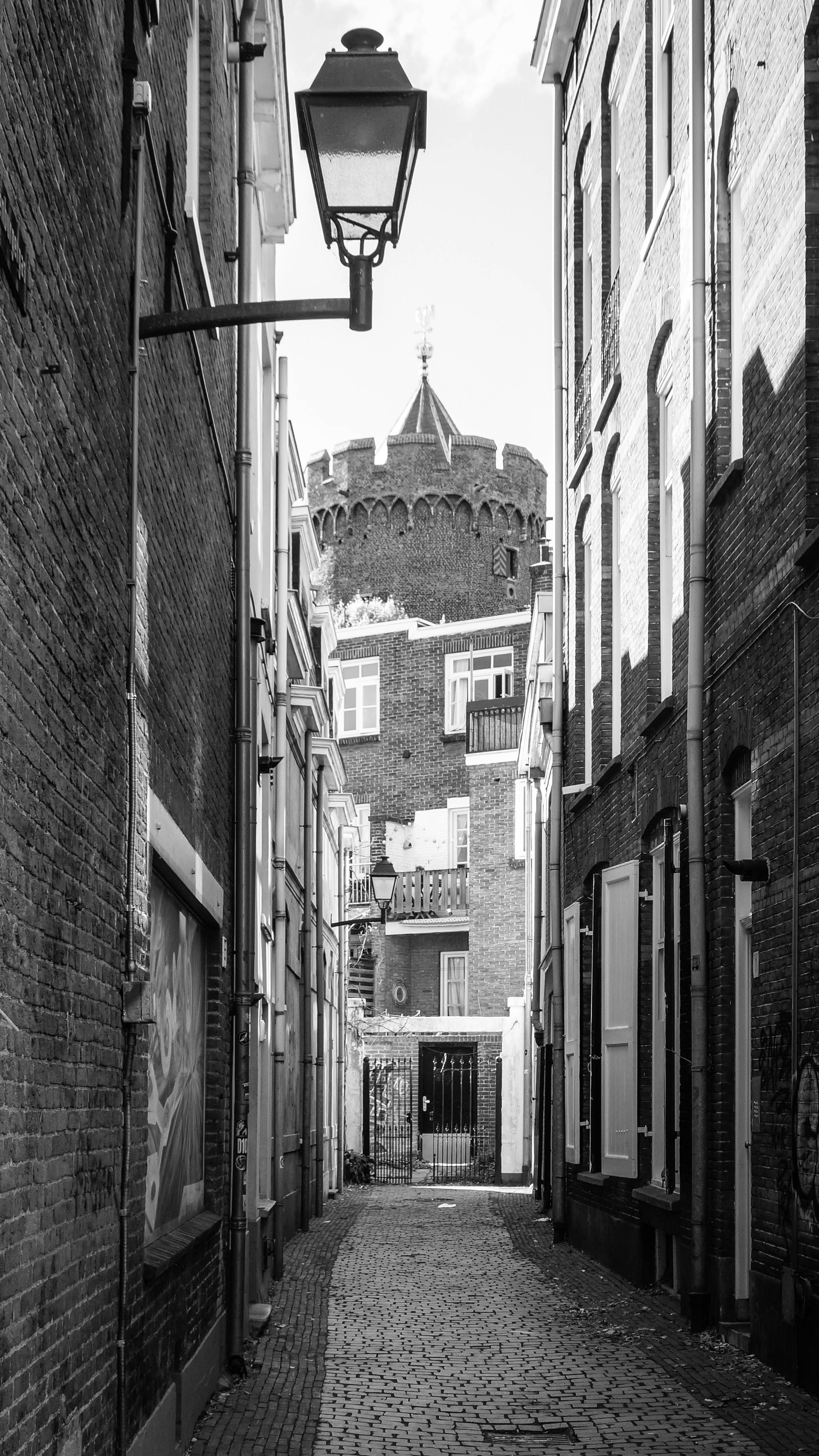 Narrow cobblestone alley with historic turret in black and white.