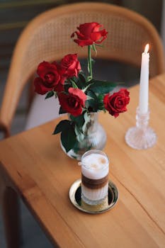 A latte with red roses and candle on a wooden table captures a cozy and romantic ambiance.