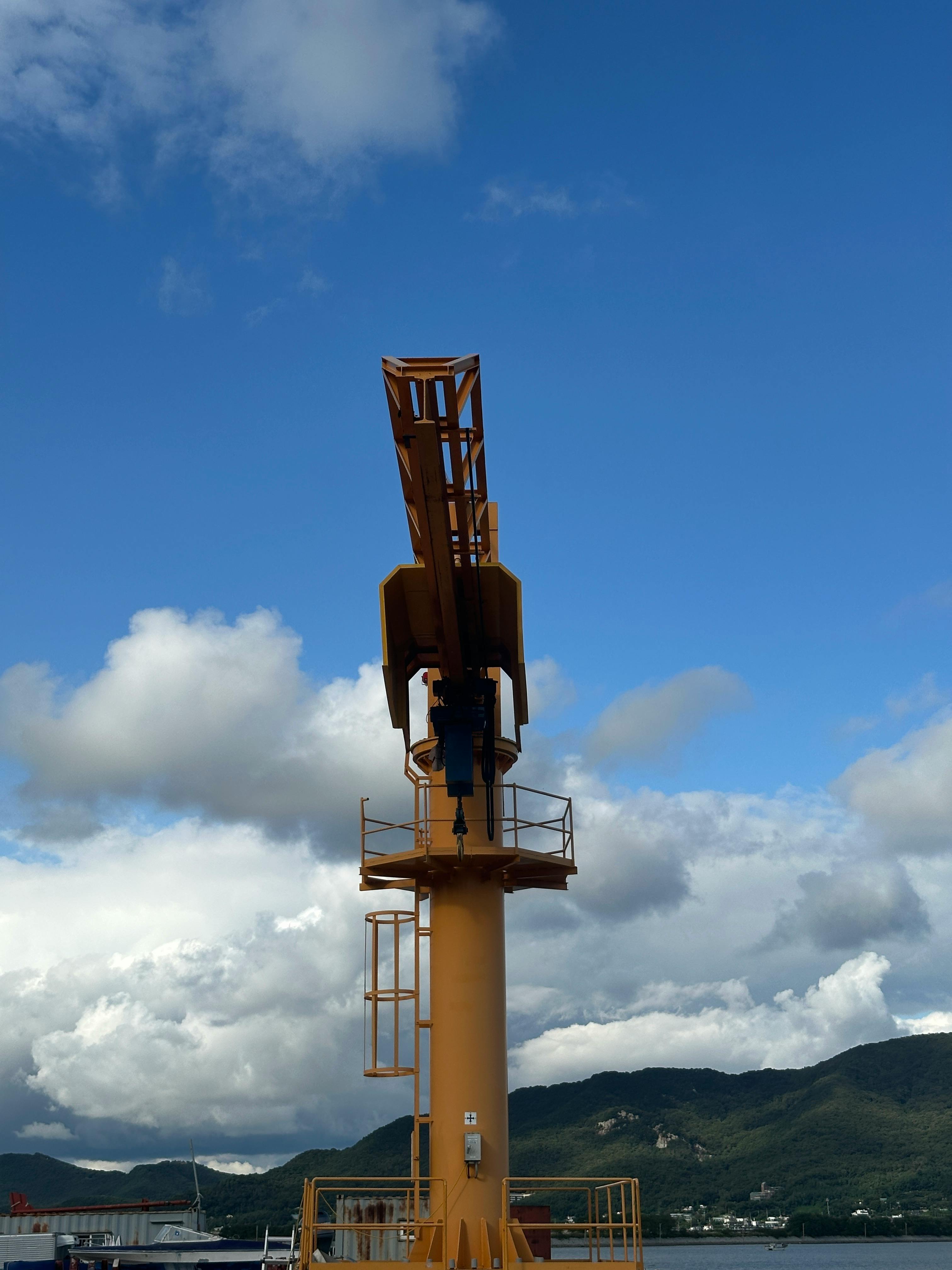 Tall yellow crane set against dramatic clouds and blue sky in an industrial port setting.