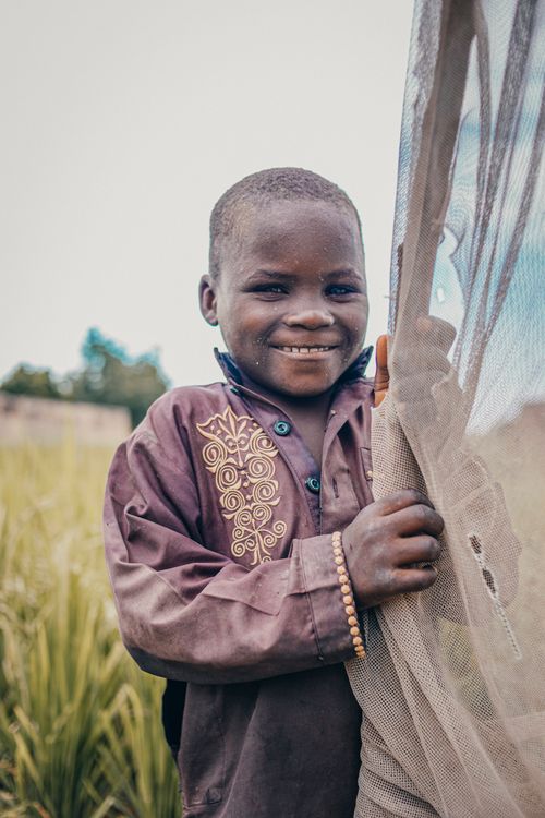 Free A young boy in traditional clothing smiles while holding a net in a rural Nigerian field. Stock Photo