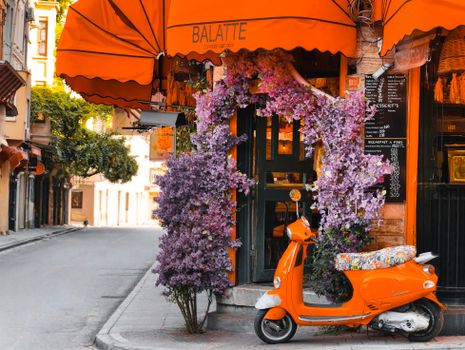 A vibrant cafe in Istanbul featuring orange decor and a scooter under a lush, floral archway.