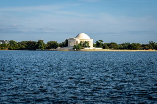 Free A serene view of the Jefferson Memorial with a clear blue sky and water reflecting its grandeur. Stock Photo