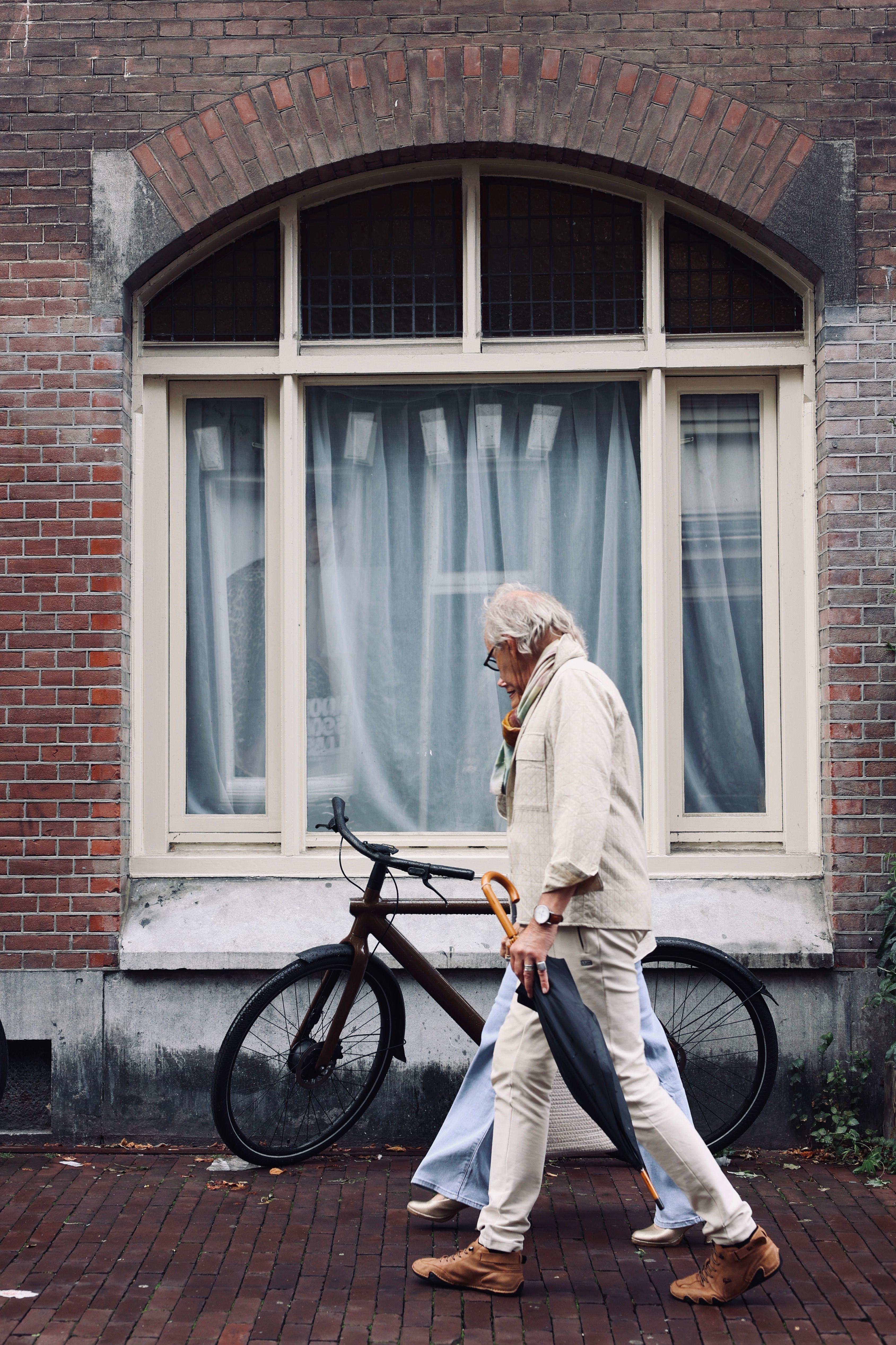 Elderly couple stroll past a bicycle against a brick building backdrop.