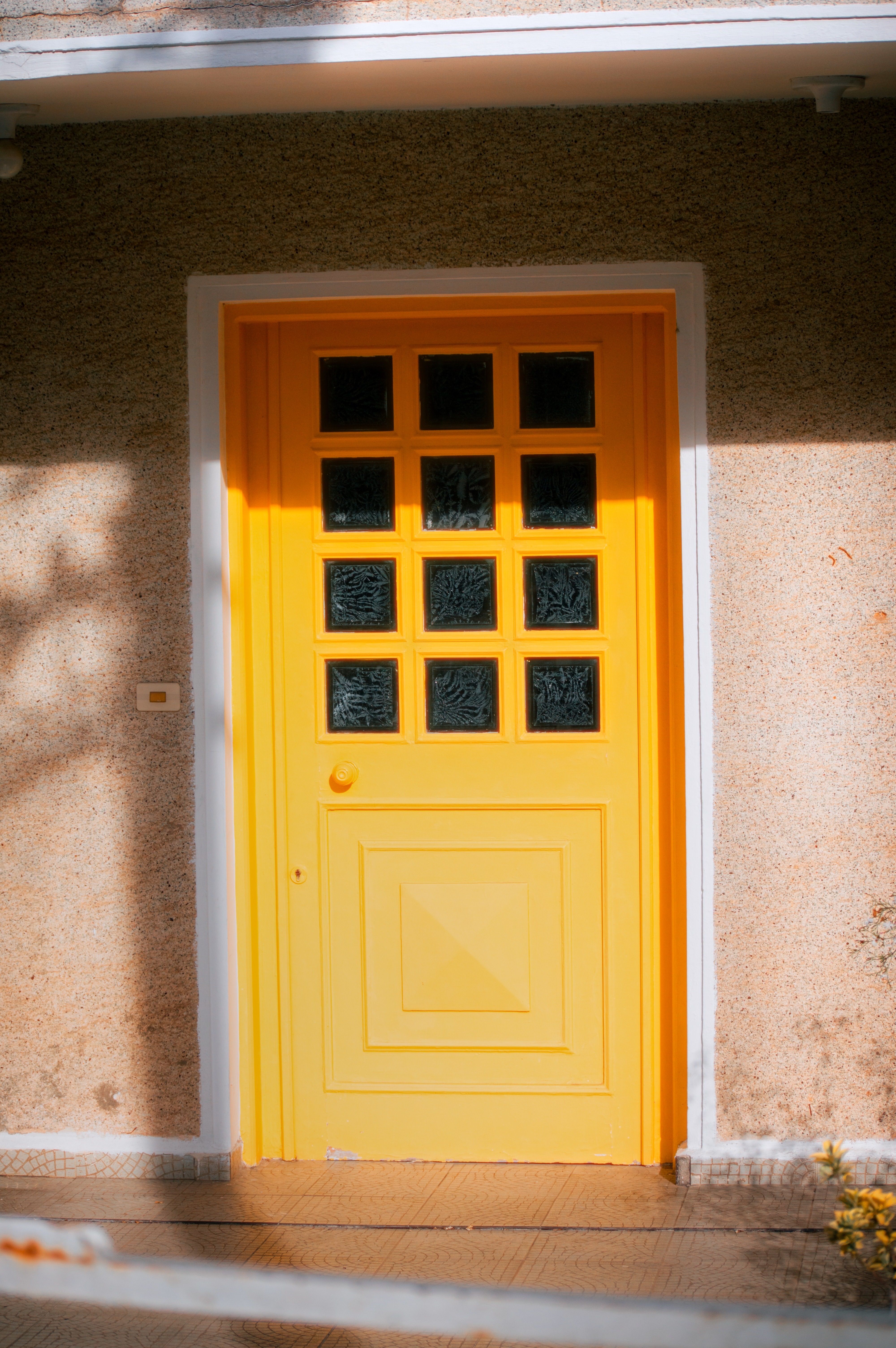Bright yellow door with glass panes and sunlight shadows on textured wall.