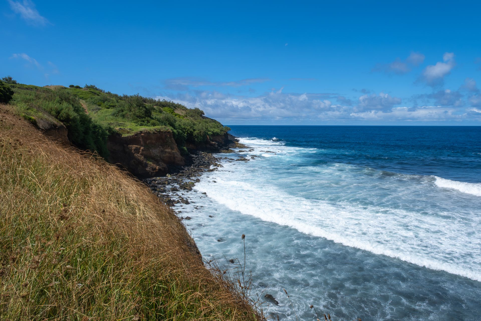 Breathtaking view of ocean waves crashing against rugged cliffs under a clear blue sky.