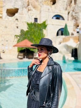Elegant woman in black by a pool, showcasing a fusion of modern fashion and charming outdoor setting.