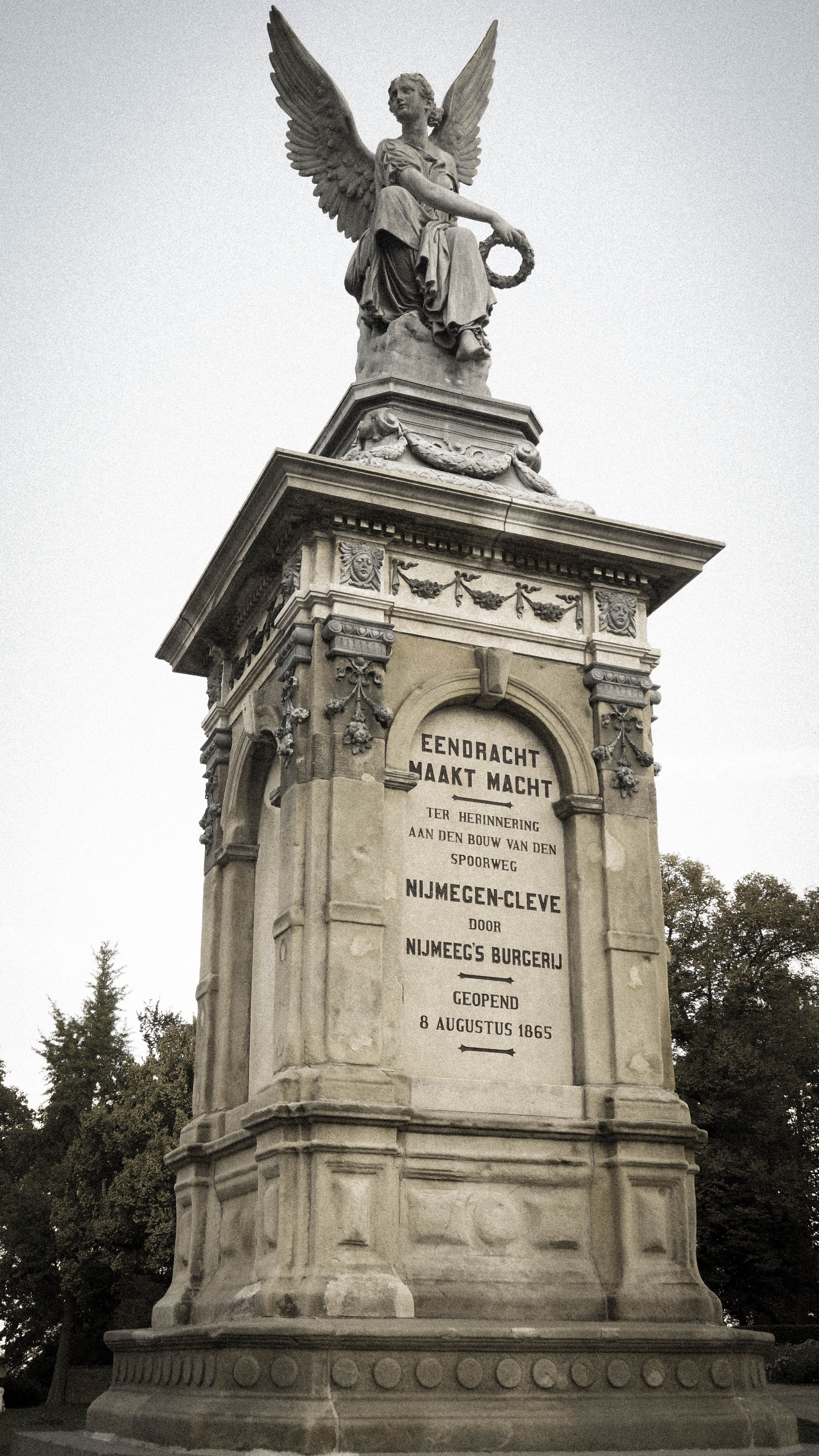 A historic angel statue atop a monument in a Nijmegen park during daytime.