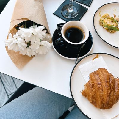Overhead café table with espresso, a croissant and white flowers — photo by N G on Pexels