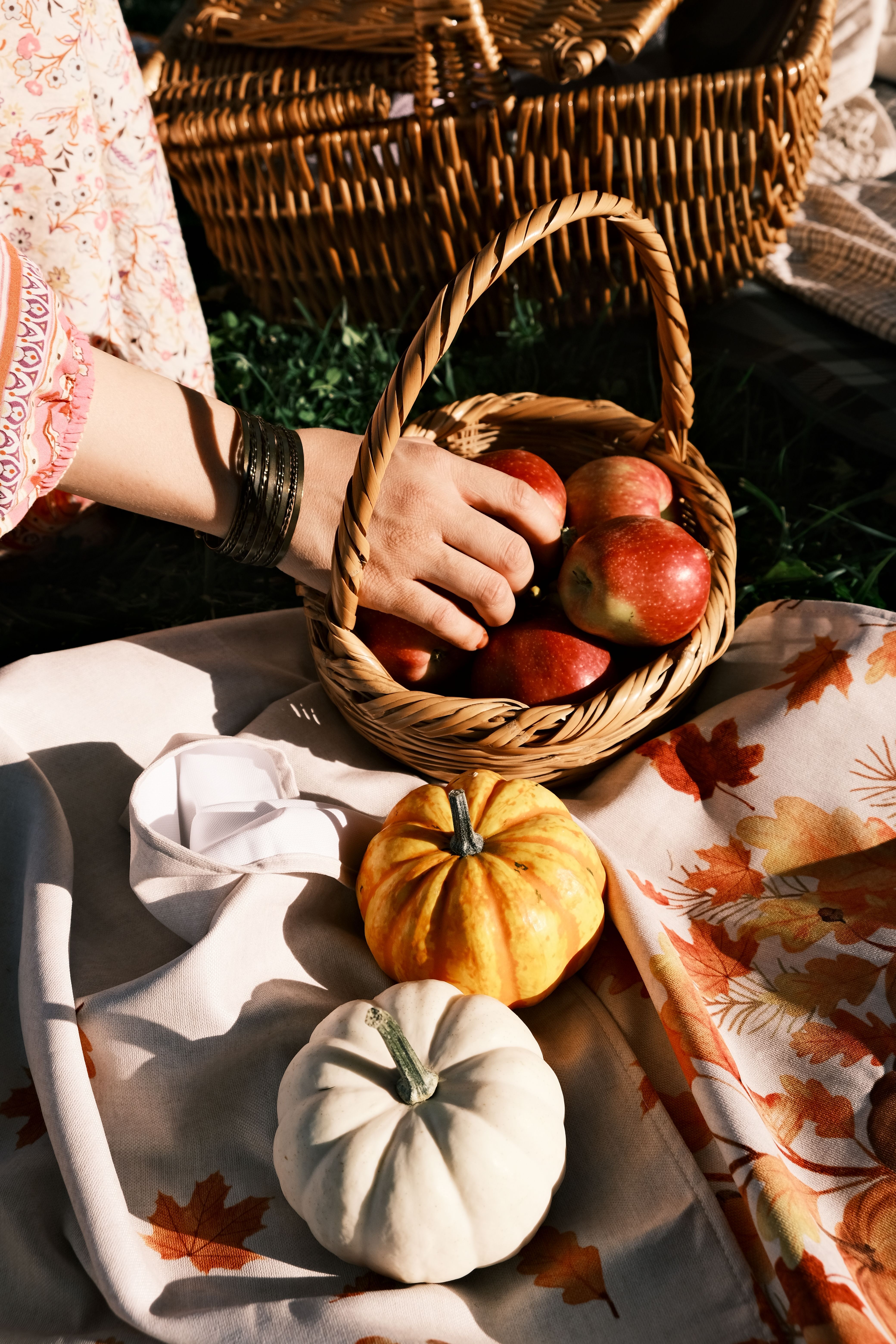 A cozy autumn picnic with a wicker basket of apples and decorative pumpkins on a blanket.