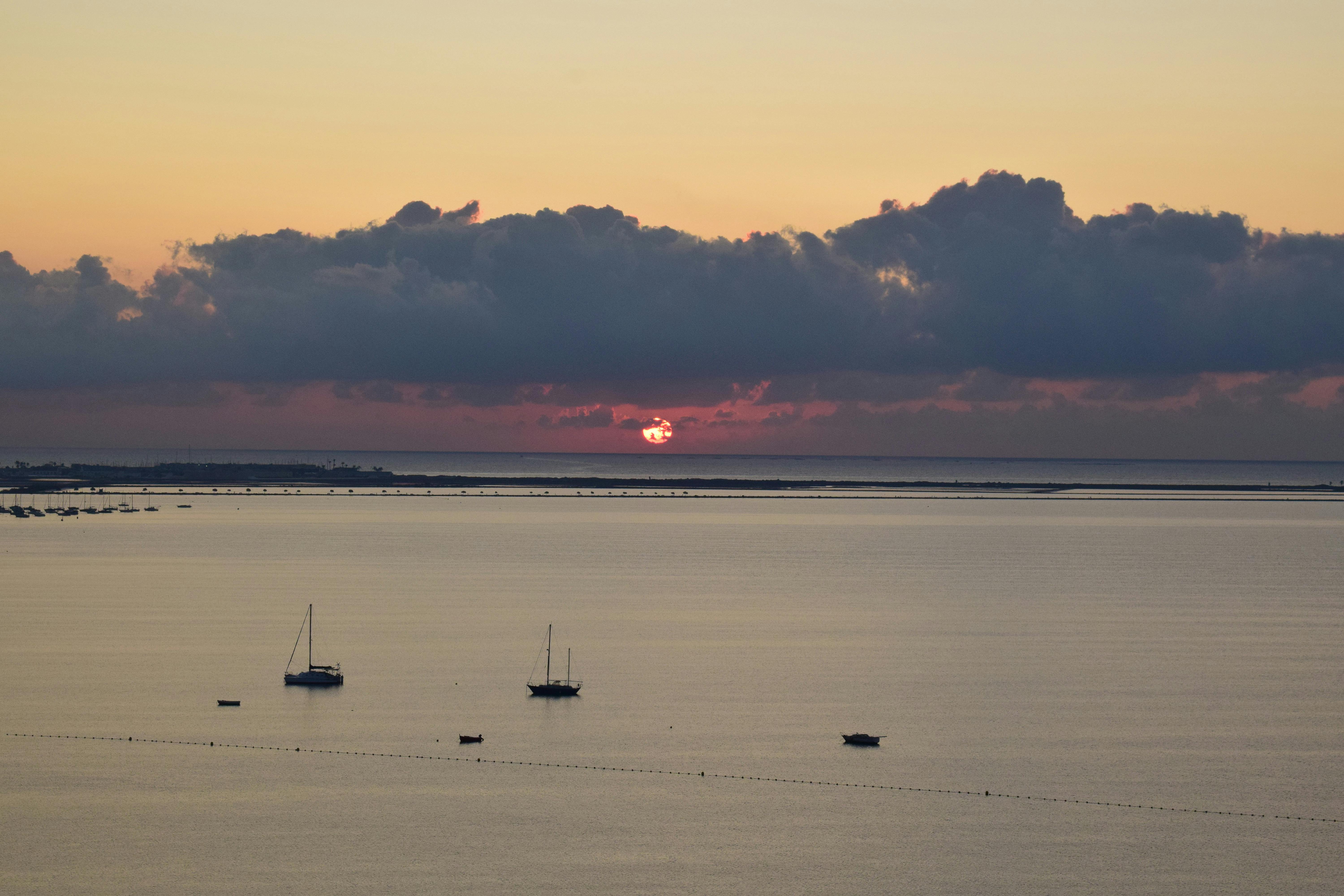 Serene sunset view over Mar Menor with sailboats and dramatic clouds in Murcia, Spain.