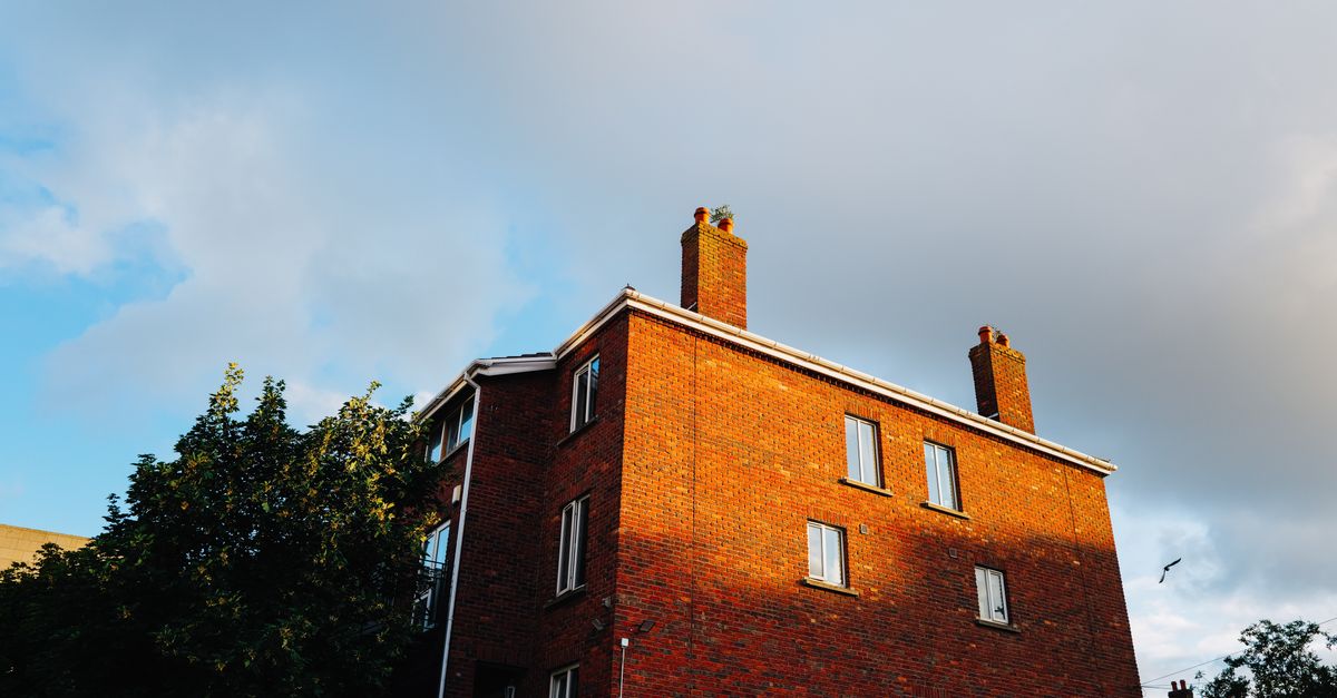 A red brick building with chimneys highlighted by sunlight against a partly cloudy sky.