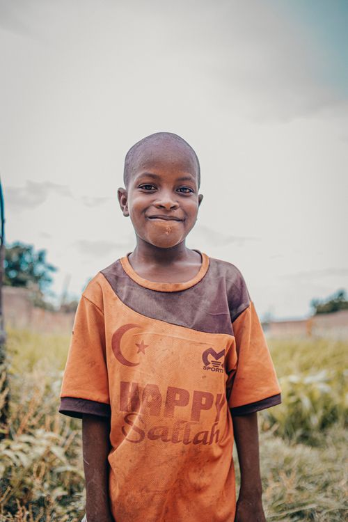 Free Smiling child in a vibrant orange t-shirt standing happily in a field. Stock Photo