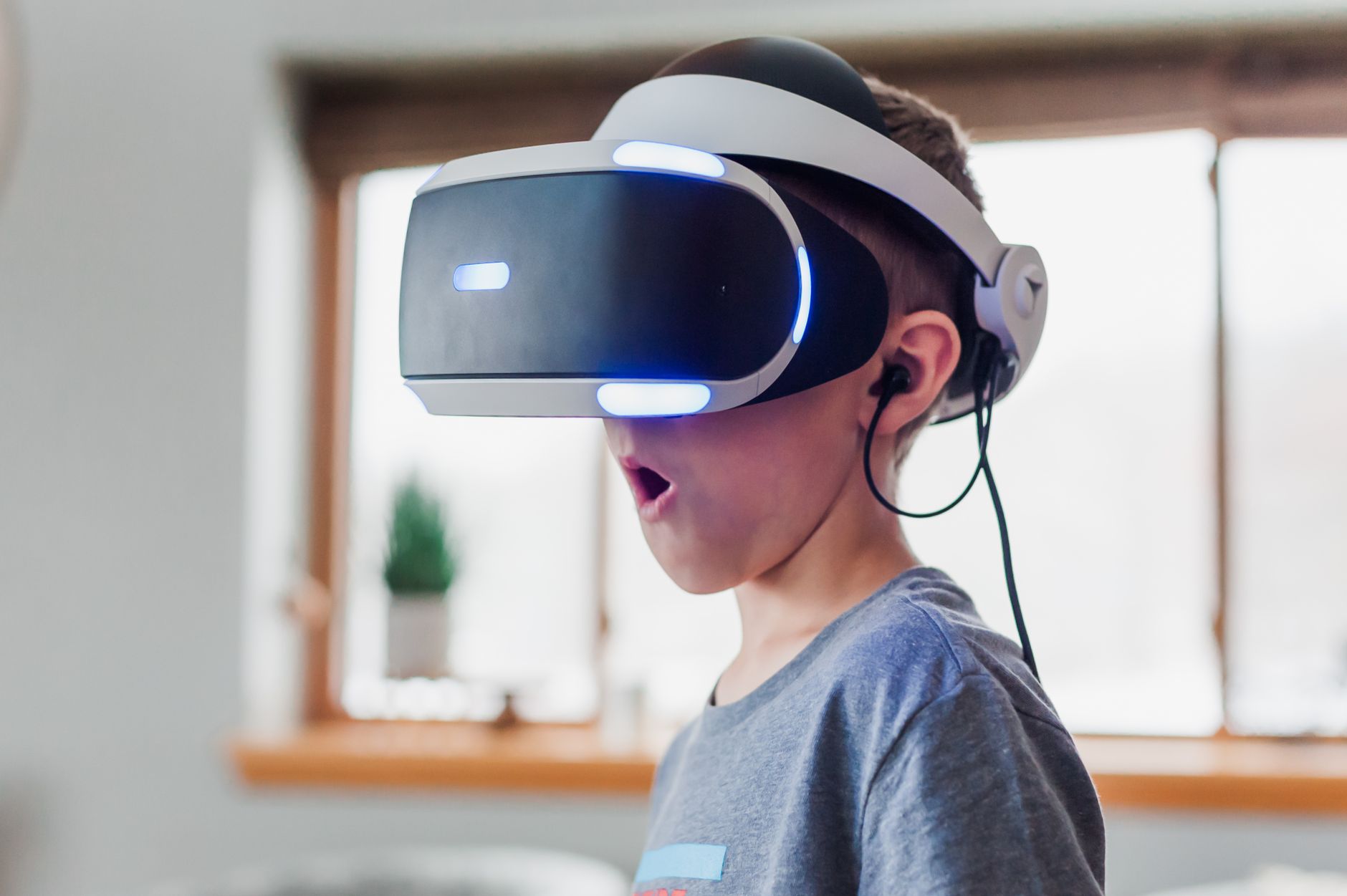 Young boy using VR headset indoors, exploring virtual reality with amazement and curiosity.