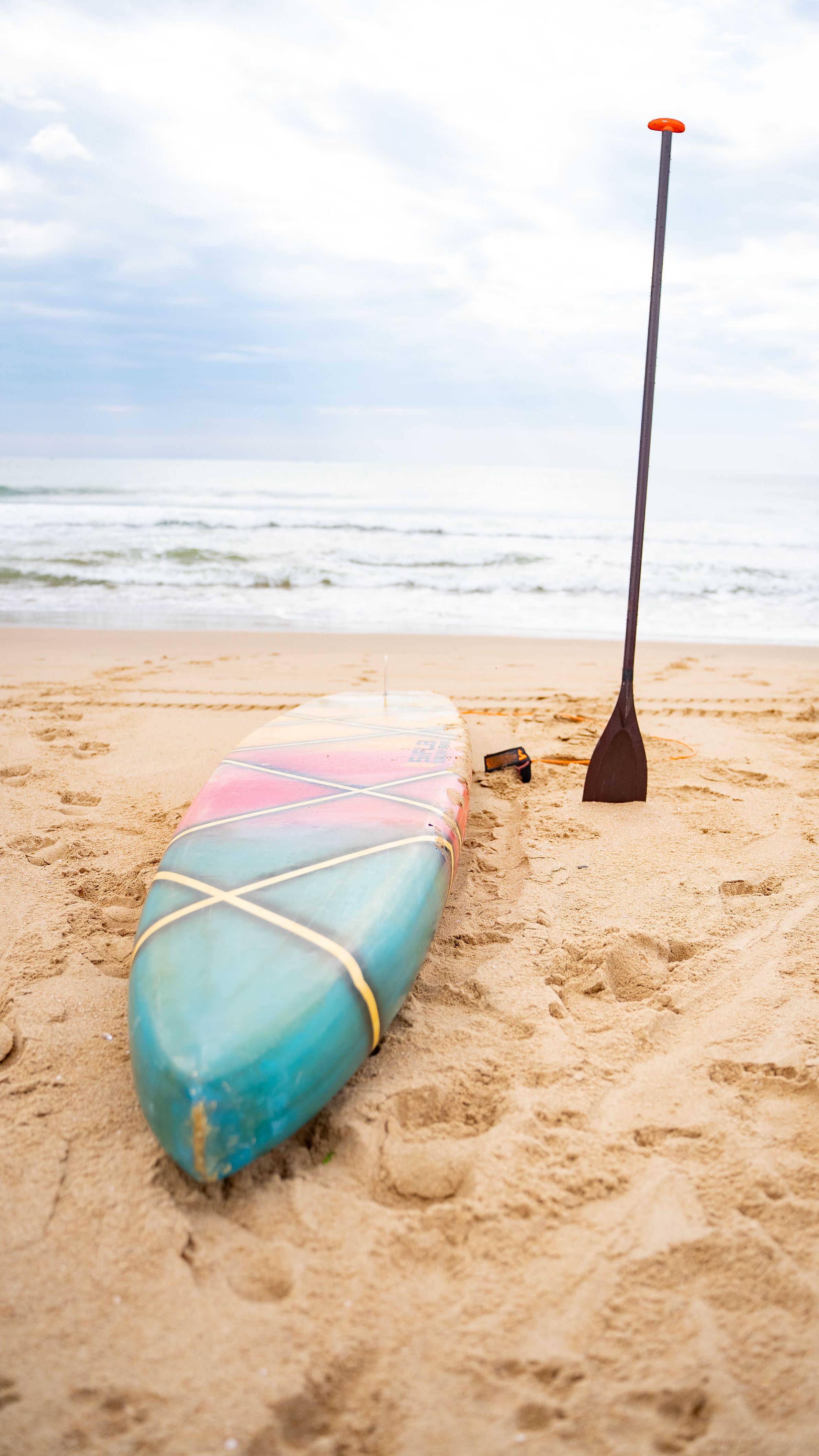 Colorful paddle board and paddle resting on clean beach sand